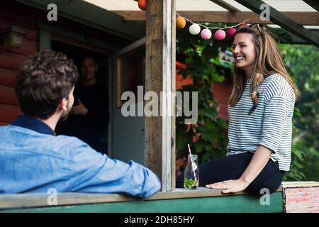 Glückliche Frau, die mit einem Freund auf der Veranda in der Blockhütte sitzt Stockfoto