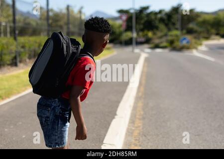 Schuljunge, die auf der Suche nach Verkehrsbehinderungen sind, während sie auf die Straße warten Stockfoto