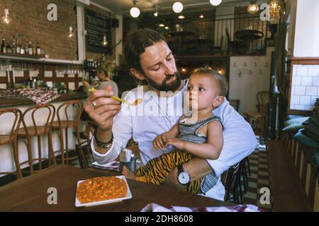Mittlerer Erwachsener Mann Fütterung Baby Junge am Restauranttisch Stockfoto