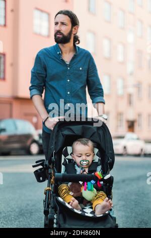 Mittelerwachsener Mann, der das Baby auf dem Bürgersteig in die Kutsche schiebt Stockfoto