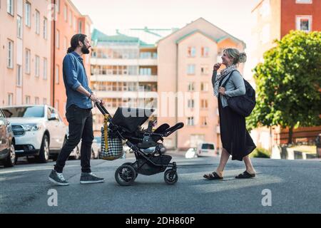 Volle Länge Seitenansicht der Eltern mit Baby und Kinderwagen überqueren Stadtstraße Stockfoto