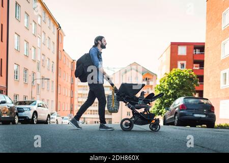 Volle Länge Seitenansicht des Mannes, der Baby in den Wagen schiebt Über die Stadtstraße Stockfoto