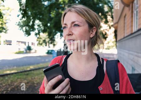 Frau mit mittlerem Erwachsenenalter, die beim Gehen auf dem Mobiltelefon spricht Gehweg Stockfoto