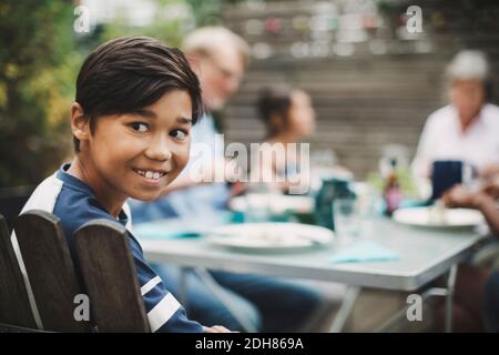 Glücklicher Junge, der wegschaute, während er mit der Familie beim Essen saß Tisch im Hof Stockfoto