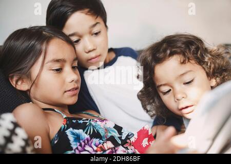 Brüder und Schwester, die zu Hause ein digitales Tablet auf dem Sofa benutzen Stockfoto