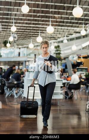 Geschäftsmann, der Smartphone benutzt, während er am Flughafen läuft Stockfoto