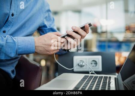 Mittelteil eines Geschäftsmannes, der in der Flughafenlobby ein Smartphone benutzt Stockfoto