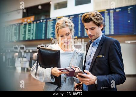 Geschäftsleute, die ein Smartphone benutzen, während sie den Reisepass betrachten flughafen Stockfoto