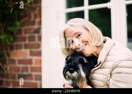 Porträt einer glücklichen älteren Frau mit Hund vor dem Haus Stockfoto