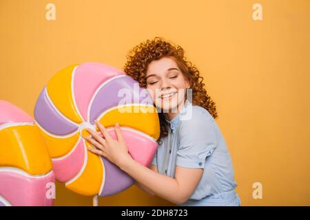 Lollipop, Ich liebe dich. Sehr glücklich rothaarige Frau umarmt Lollipop Süßigkeiten, auf orangefarbenem Hintergrund Stockfoto