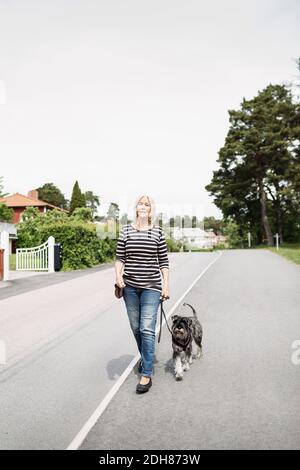 Volle Länge der älteren Frau zu Fuß mit Hund auf der Straße Stockfoto