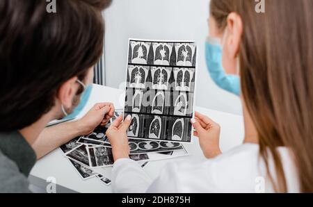 Der Pneumologe trägt eine Schutzmaske und zeigt dem Patienten einen CT-Scan seiner Lunge. Lungenentzündung, Coronavirus, Lungenerkrankung Stockfoto