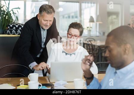 Geschäftsmann und Frau, die in einem Laptop sitzen, während sie am Tisch sitzen Stockfoto