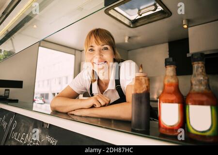 Porträt einer glücklichen Köchin, die sich auf der Theke beim Essen stützt LKW Stockfoto