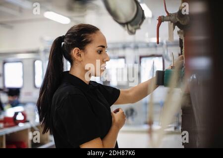 Seitenansicht der weiblichen Auto-Mechaniker Student Analyse Maschinen bei Werkstatt Stockfoto
