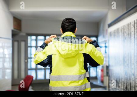 Rückansicht Auto Mechaniker Schüler trägt reflektierende Jacke in Werkstatt Stockfoto