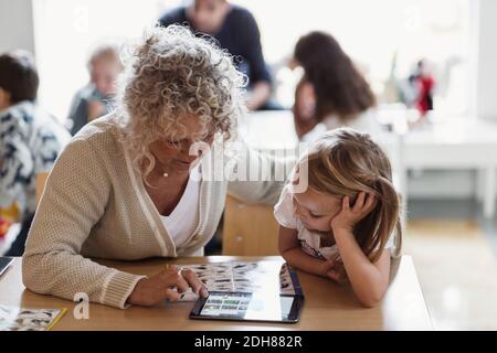 Oberlehrer mit digitalem Tablet mit Schüler im Kindergarten Stockfoto