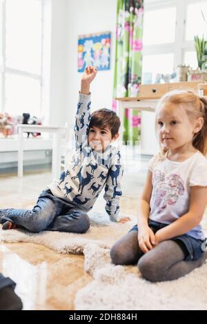 Happy boy Heben Hand, während sitzend von Mädchen im Klassenzimmer Stockfoto