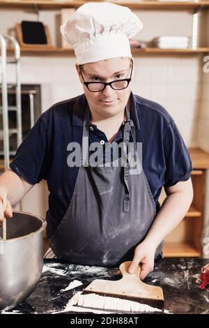 Portrait des jungen Mannes, der Teig in der kommerziellen Küche macht Stockfoto