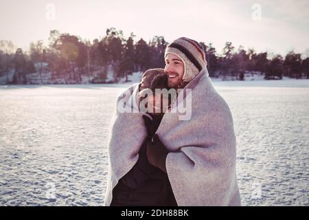 Lächelndes Paar in Decke gewickelt, während auf dem Feld stehend während Winter Stockfoto