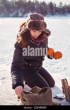 Frau hält Orangen, während sie auf schneebedecktem Feld kniet Stockfoto