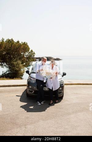 Pärchen steht vor dem Auto und schaut auf das nächste Ziel Für Reisen in der Karte Stockfoto