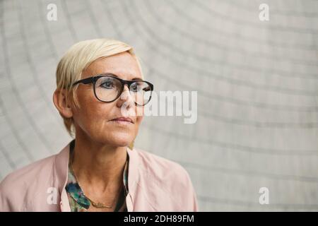 Nachdenkliche Geschäftsfrau mit Brillen an der Wand Stockfoto