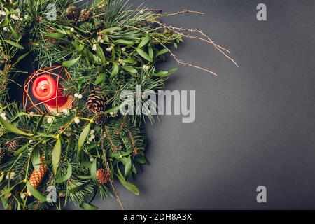 Weihnachts- und Neujahrskranz aus Tanne, Kiefer, Mistelzweigen, Zapfen mit brennender Kerze im Inneren. Öko und natürliche Dekoration Stockfoto