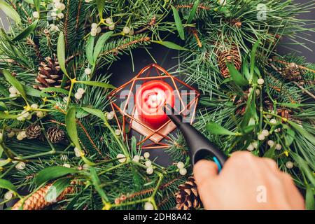 Frau leuchtet Kerze im Inneren Weihnachten und Neujahr Kranz aus Tanne, Kiefer, Mistelzweigen, Zapfen. Öko und natürliche Dekoration Stockfoto