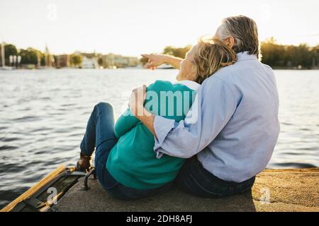 Älterer Mann, der der Frau etwas zeigt, während er auf dem Pier sitzt Stockfoto