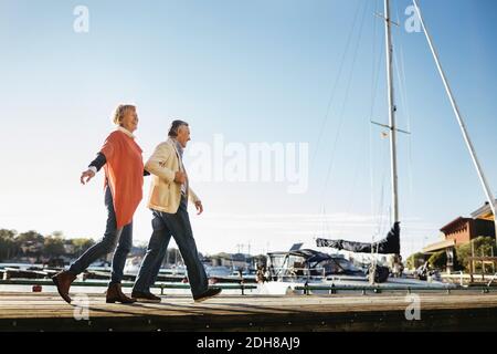 Ein glückliches Paar, das auf dem Pier gegen den Pier läuft Himmel Stockfoto