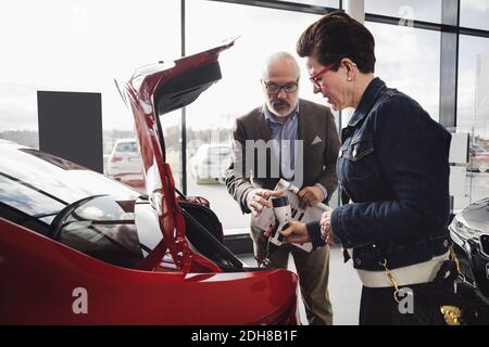 Ältere Mann und Frau untersuchen Ladegerät des Elektroautos bei Ausstellungsraum Stockfoto