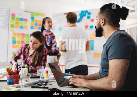 Geschäftsmann, der am Laptop arbeitet, mit Kollegen im Hintergrund im Büro Stockfoto