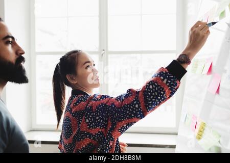 Ingenieurin schreibt auf Whiteboard und erklärt Kollegen im Büro Stockfoto