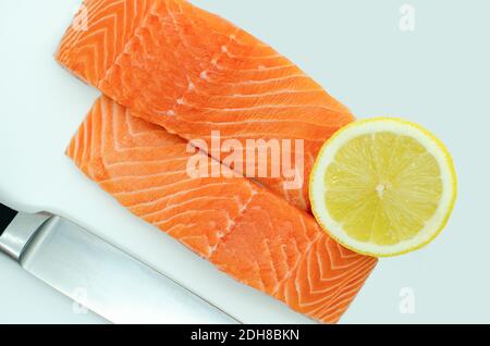 Zwei Scheiben frisches Lachsfilet, Draufsicht weißer Hintergrund. Messer und Zitrone Stockfoto