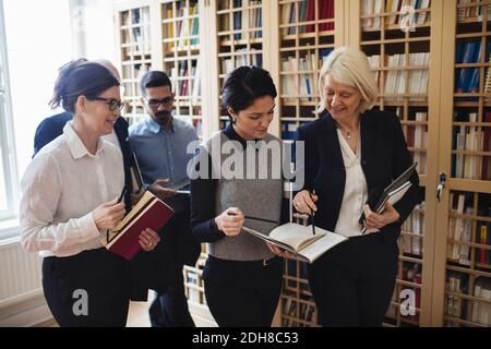 Lächelnde Anwälte diskutieren beim Spaziergang durch Bücherregal in der Bibliothek Stockfoto