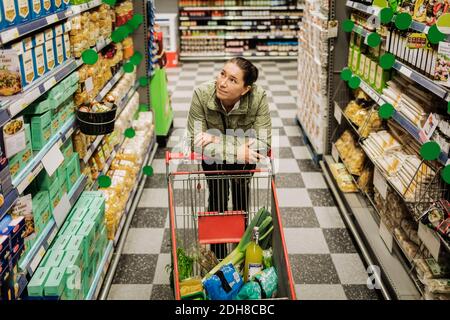 High-Angle-Ansicht der nachdenklichen Frau lehnt sich auf den Warenkorb Im Supermarkt Stockfoto