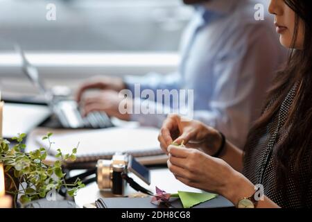Zugeschnittenes Bild von Frau Herstellung Origami während sitzen von Mitarbeiter Im kreativen Büro Stockfoto