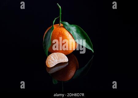 Köstliche und schöne Mandarinen mit grünem Blatt. Geschälte Mandarine orange und Mandarine orange Scheiben auf einer dunklen reflektierenden Oberfläche. Stockfoto