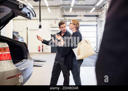 Mechaniker, der weibliche Kundin bei der Nutzung der mobilen App im Auto unterstützt Reparaturwerkstatt Stockfoto