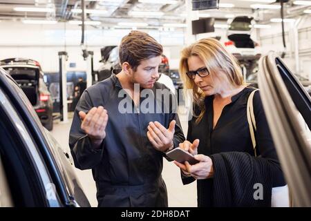 Mechaniker, der den Kunden bei der Verwendung der mobilen App bei der Autoreparatur unterstützt Kaufen Stockfoto