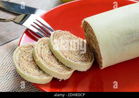 Nahaufnahme von geschnittenem Bolo de rolo (Rollkuchen) auf einer roten Platte neben einer Gabel. Stockfoto