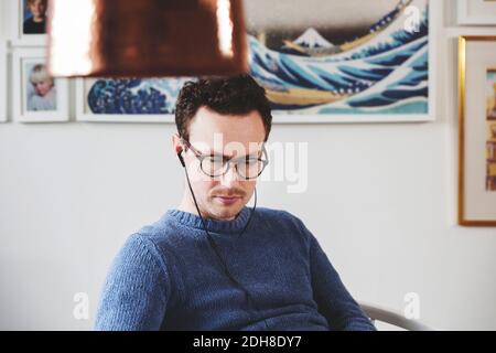 Konzentrierter Mann, der Musik hört, während er zu Hause auf dem Stuhl sitzt Stockfoto