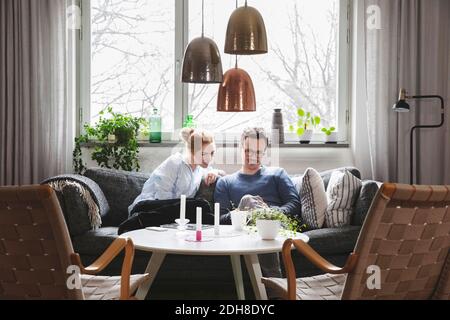 Ein Paar schaut im Smartphone, während es zu Hause auf dem Sofa sitzt Stockfoto