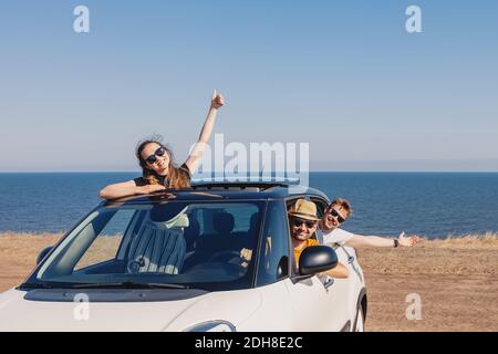 Fröhliche lächelnde Unmünder im Auto am Meer. Roadtrip im Sommer Stockfoto