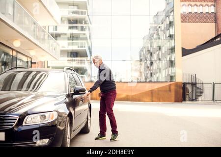 Älterer Mann, der mit dem Auto gegen Gebäude in der Stadt steht Stockfoto