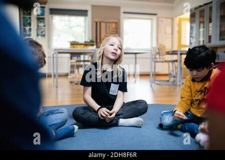 Mädchen reden, während sie mit Freunden auf dem Boden im Klassenzimmer sitzen Stockfoto