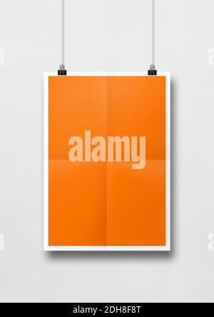 Orangefarbenes gefaltetes Poster, das an einer weißen Wand mit Clips hängt Stockfoto