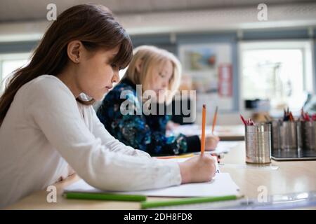 Seitenansicht der Schüler, die auf Papier schreiben, am Schreibtisch Schulungsraum Stockfoto