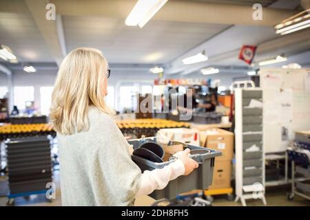 Frau mit blonden Haaren trägt Kiste in der Werkstatt Stockfoto